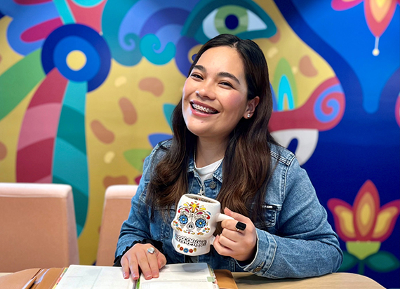 A headshot of Zayri Duenas smiling with a colorful background behind her.